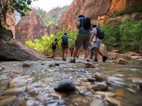 Shot from a low perspective just above the water, students walk down a river bed with reddish canyon walls on either side of them